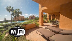 Un balcon avec des fauteuils de jardin, une piscine et une vue sur un complexe hôtelier.