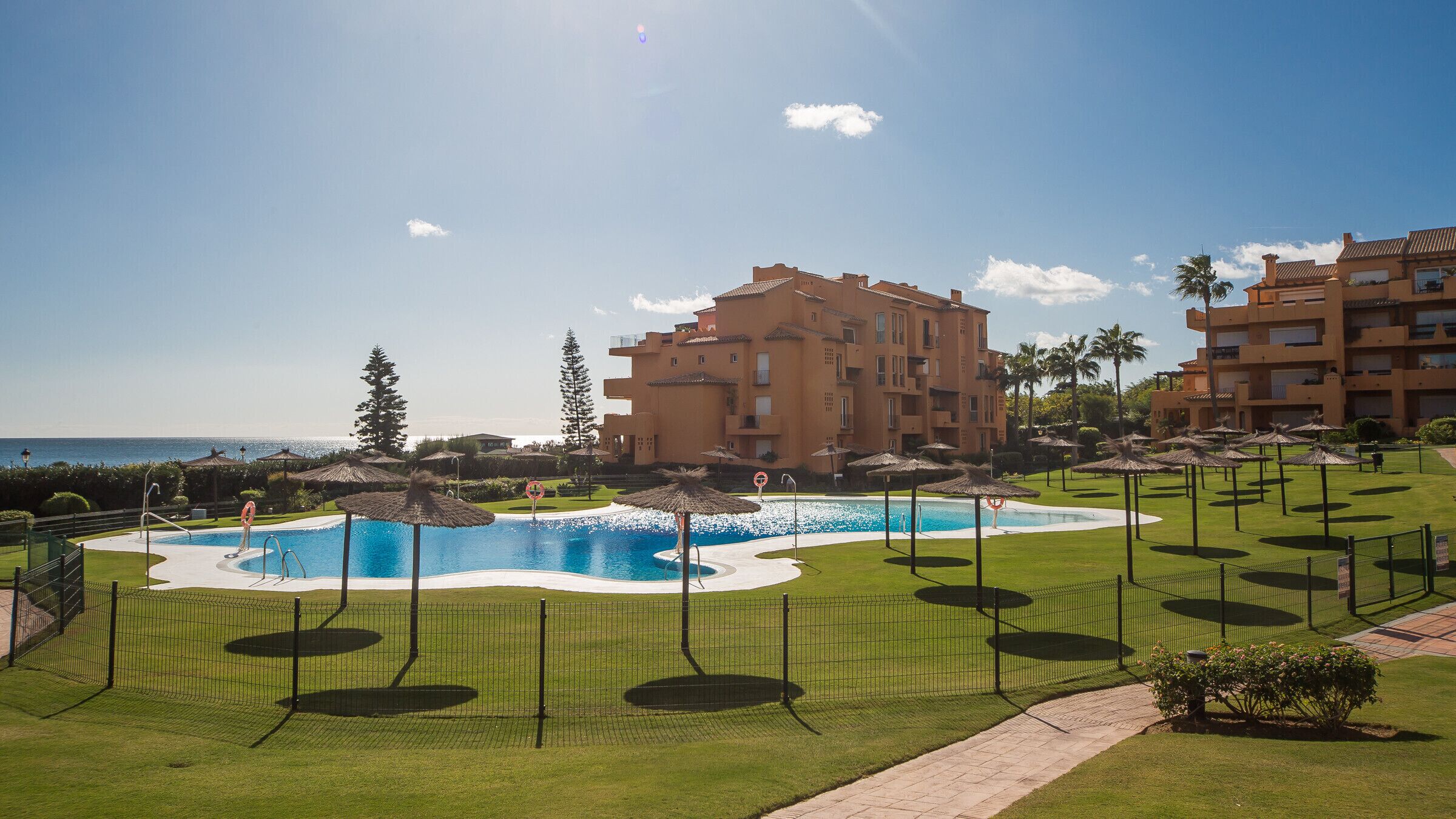 Une piscine entourée d’une clôture, avec un bâtiment en arrière-plan.
