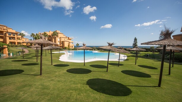 Un complexe hôtelier doté d’une piscine, de parasols en chaume et offrant une vue sur l’océan.