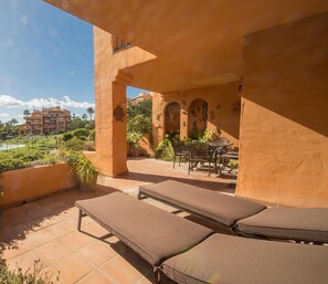 A balcony with lounge chairs, a pool, and a view of a resort complex.