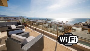Une terrasse sur le toit, aménagée avec des meubles en osier et dotée d’une rambarde en verre, offrant une vue sur la côte.