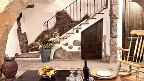 Ein Zimmer mit steinernen Wänden und einer Holztreppe, einem Esstisch mit Obstschale, Weingläsern und einer Weinflasche.