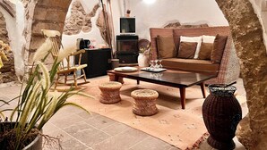Ein gemütliches Wohnzimmer mit einem Steinbogen, einem Korbsessel, einem Holztisch und einer Topfpflanze.