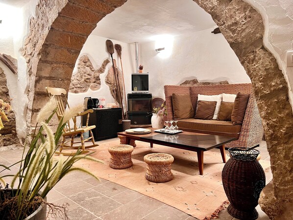 A cozy living room with a stone archway, a wicker sofa, a wooden coffee table, and a potted plant. - Casa Maria | Charm in the heart of the castle (Castelsardo)