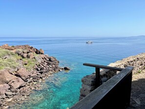 A rocky coastline with clear blue water and a wooden railing. - Casa Maria | Charm in the heart of the castle (Castelsardo)