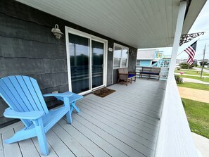 A covered porch with a blue Adirondack chair and a small table, a sliding glass door, and an American flag. - Cozy 3 Bedroom Cottage in Nags Head -- Extra Apt with BR + BA Available (Nags Head)
