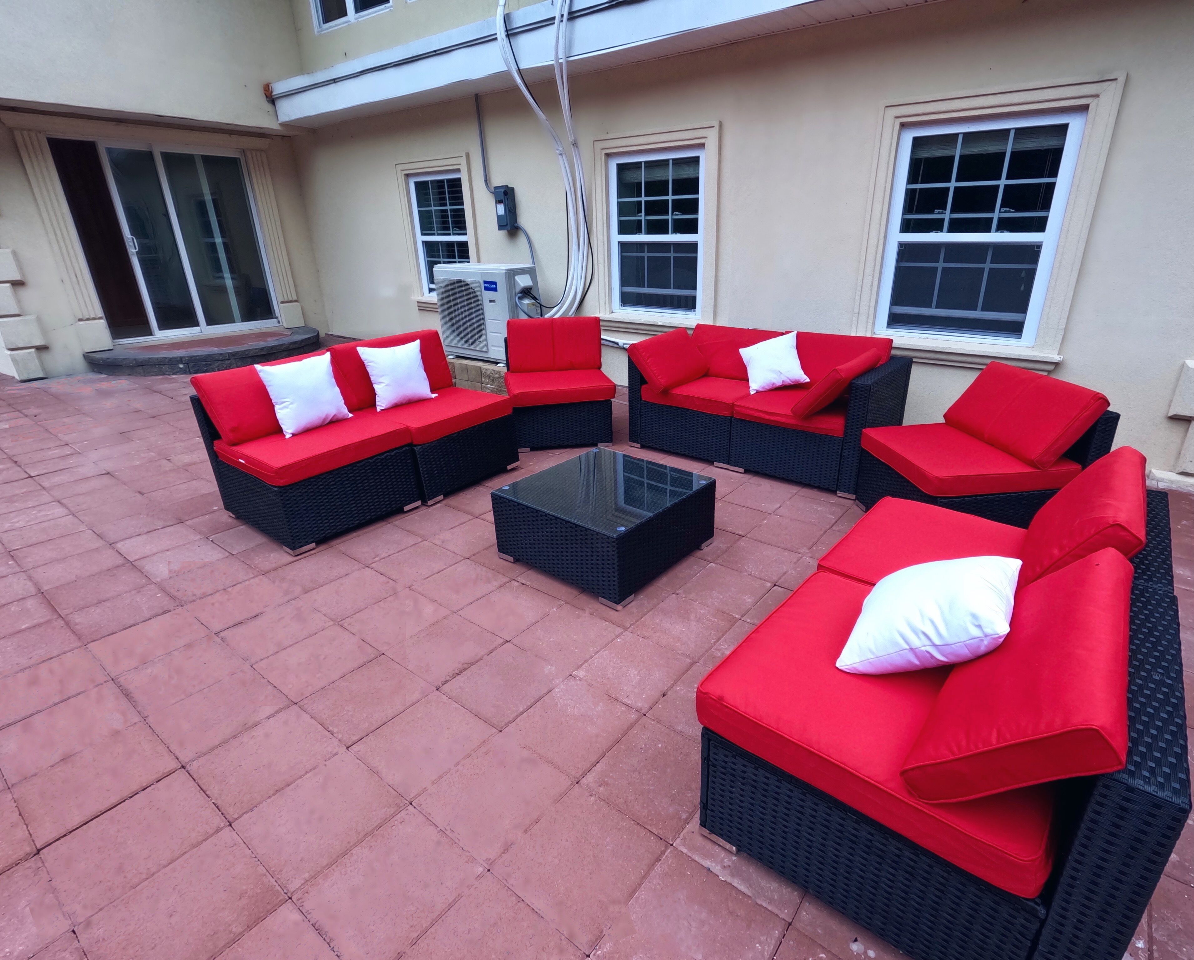 A patio with red and black wicker furniture, including sofas and a coffee table, and a tiled floor.