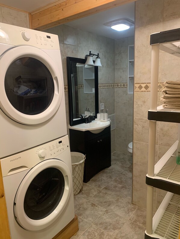 A compact laundry room with stacked washers and dryers, a sink with toiletries, and a mirror. - Cozy 4bd with the gym, sauna, hot tube seasonal pool (Greentown)
