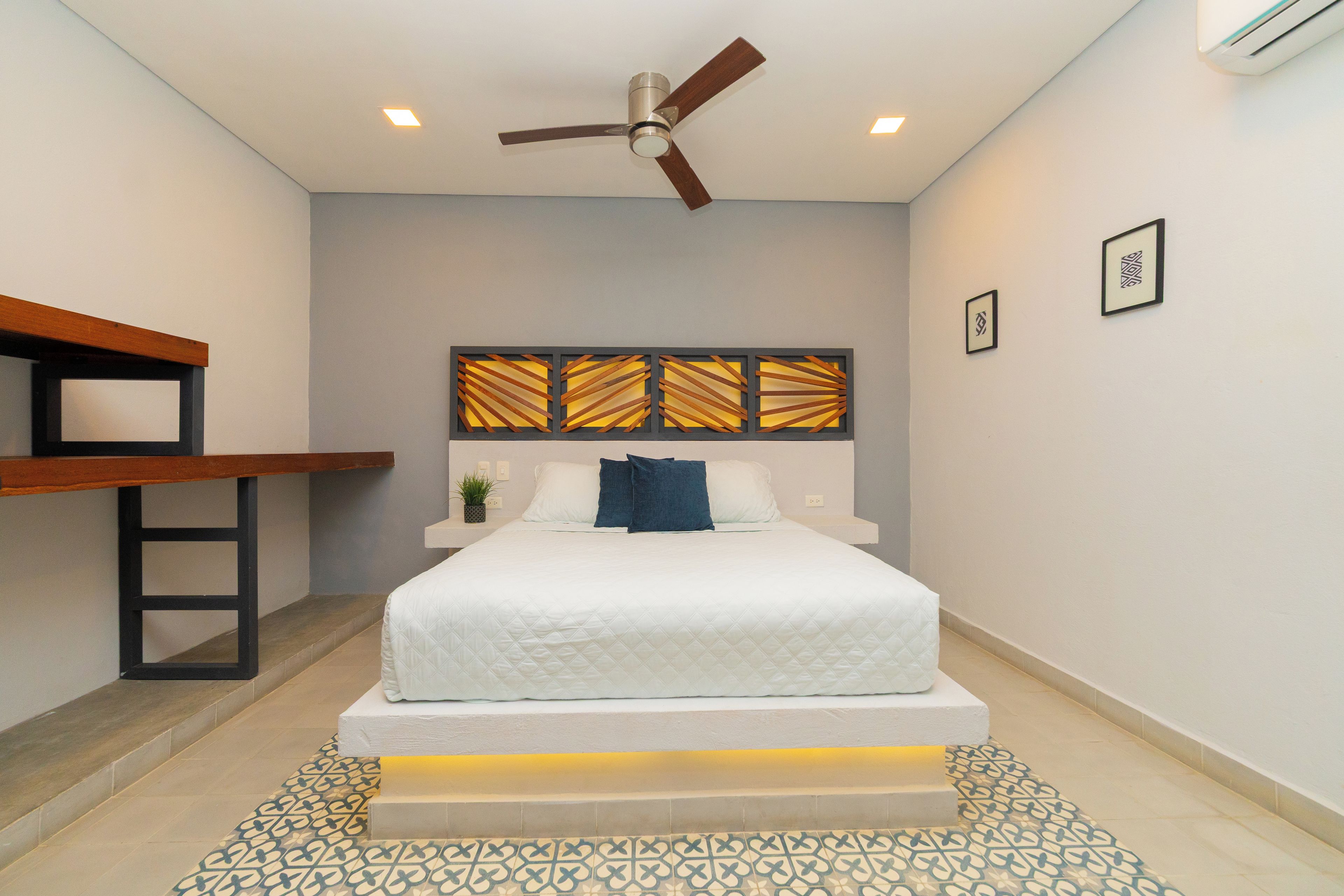 Un dormitorio con cama, escritorio, ventilador de techo e iluminación de pared.