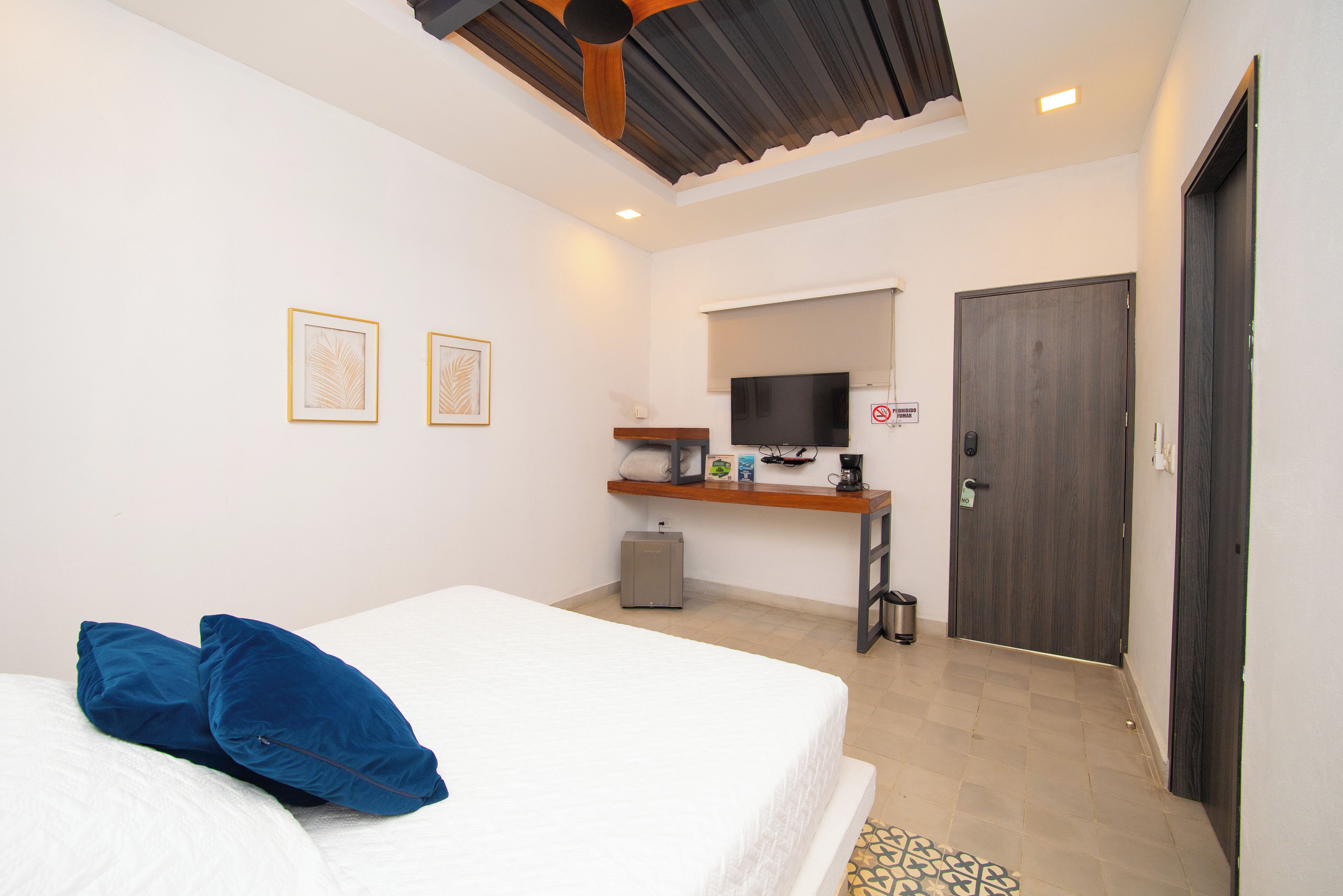 A bedroom with a bed, pillows, a desk with a TV, a coffee maker, and a door with a 'No Smoking' sign.