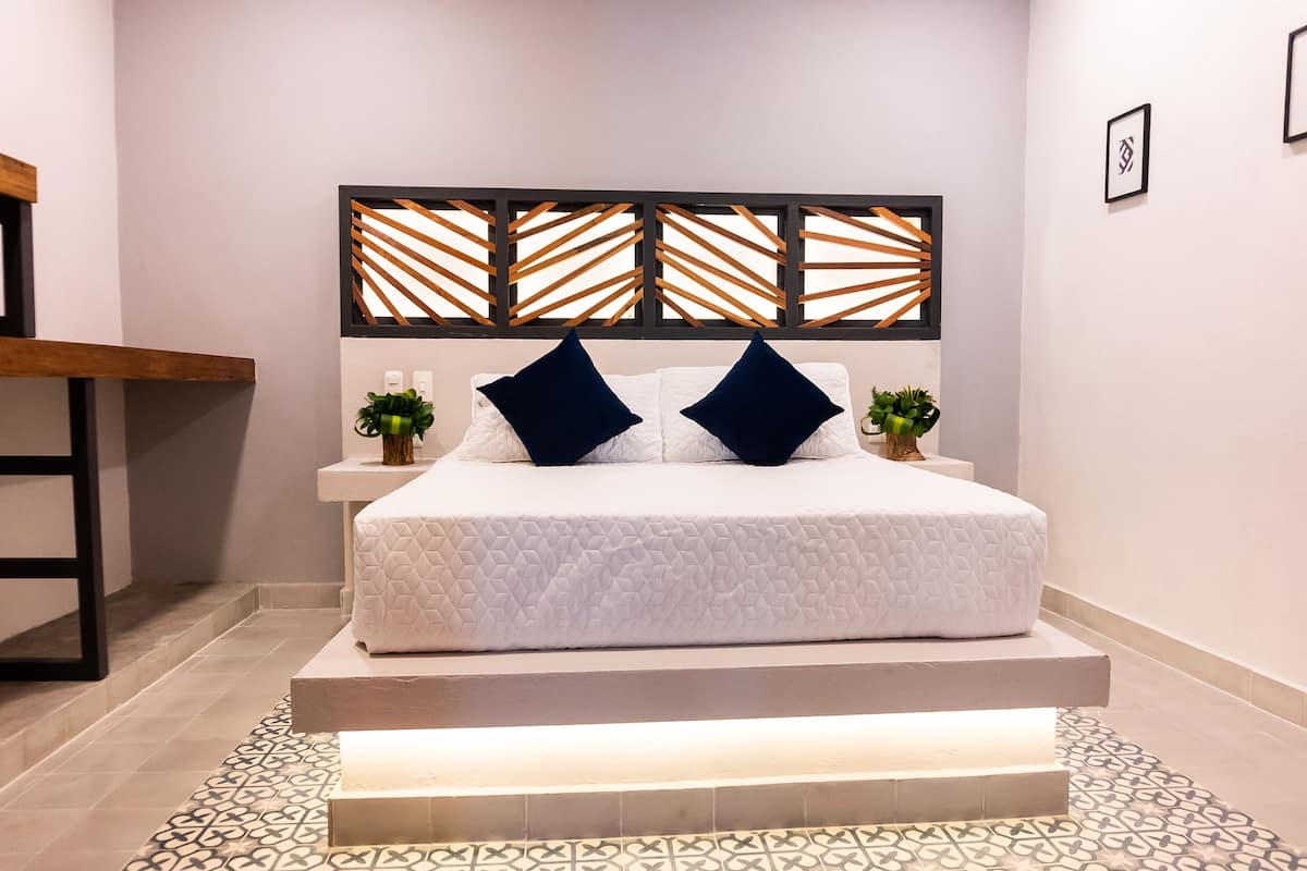 Une chambre moderne avec un lit blanc, des coussins bleu foncé et un sol à motifs géométriques.