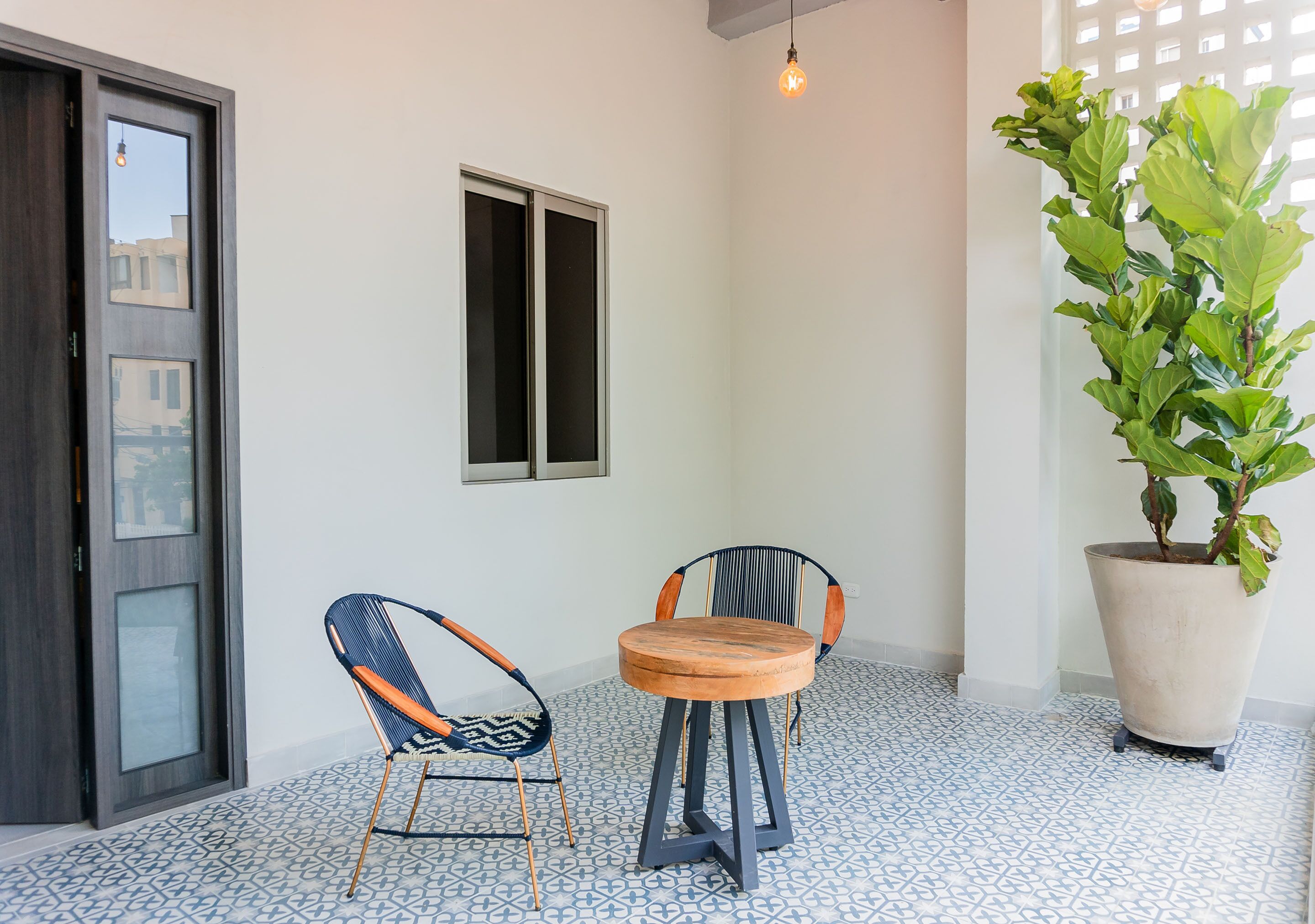A room with a round wooden table, two chairs, a potted plant, a window, and a door.