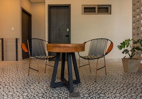 Una habitación con una mesa redonda de madera y dos sillas con estructura metálica y cojines estampados. Hay una planta en maceta en el suelo.