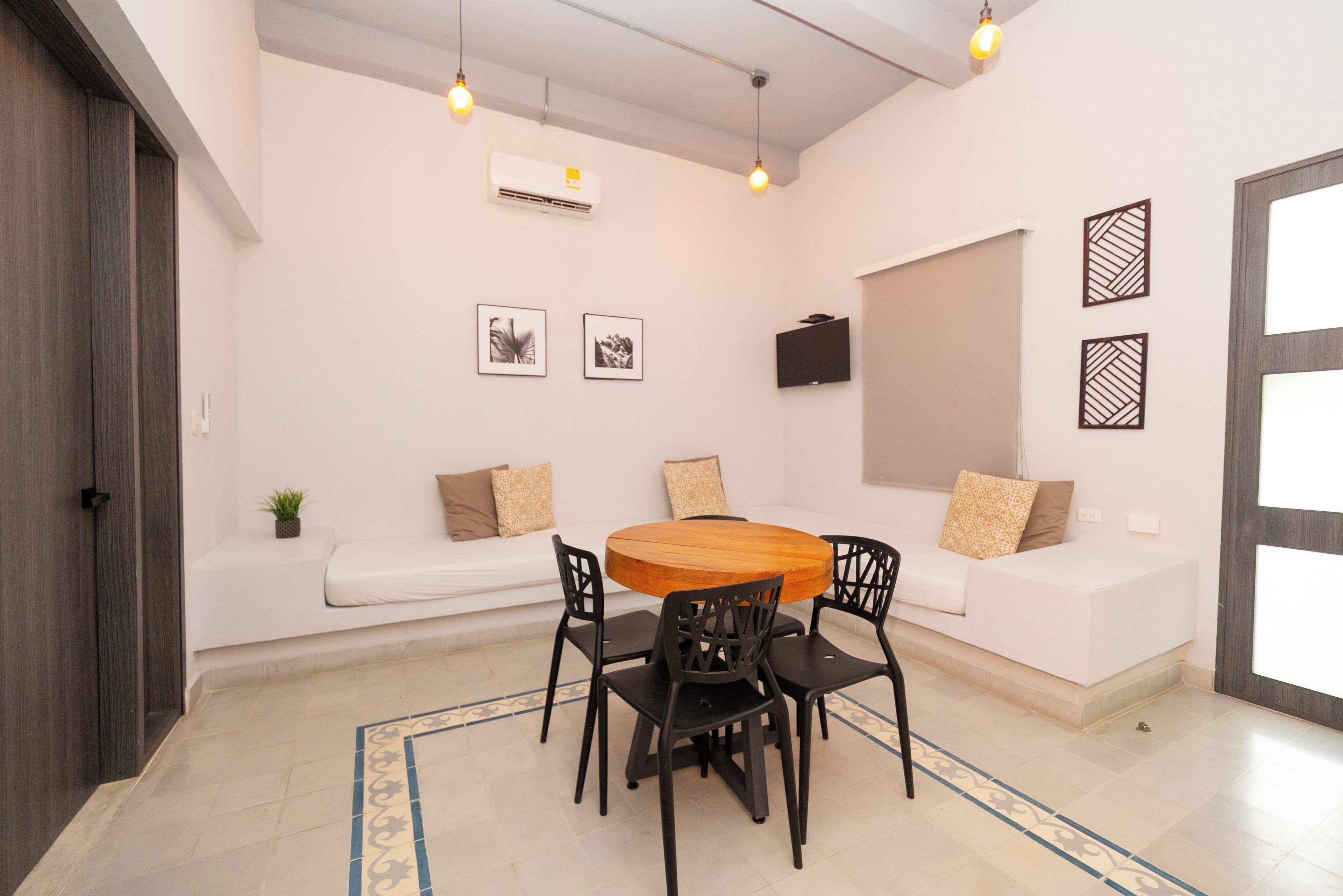Un'area pranzo moderna con un tavolo rotondo in legno, sedie nere e un divano bianco con cuscini decorati.