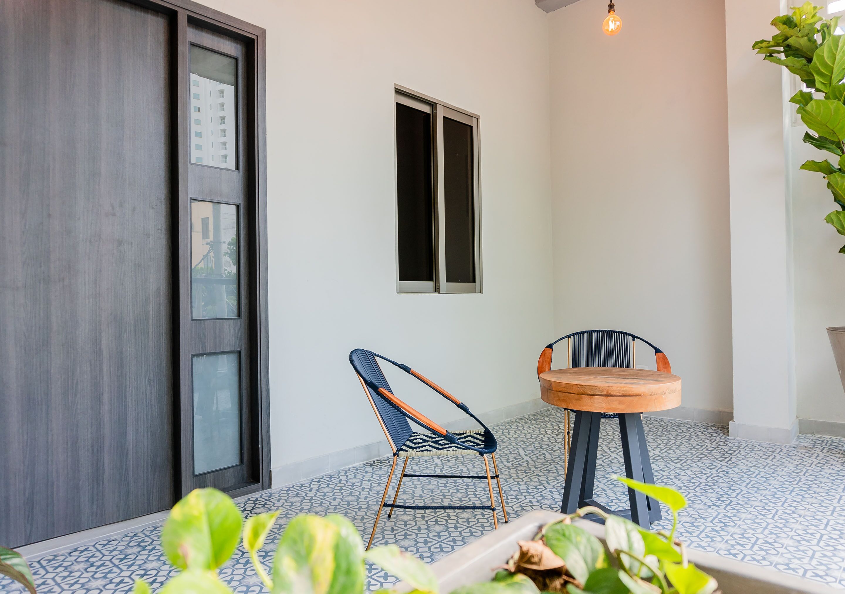 A room with a dark wooden door, a window, two chairs, a small round table, and a potted plant.