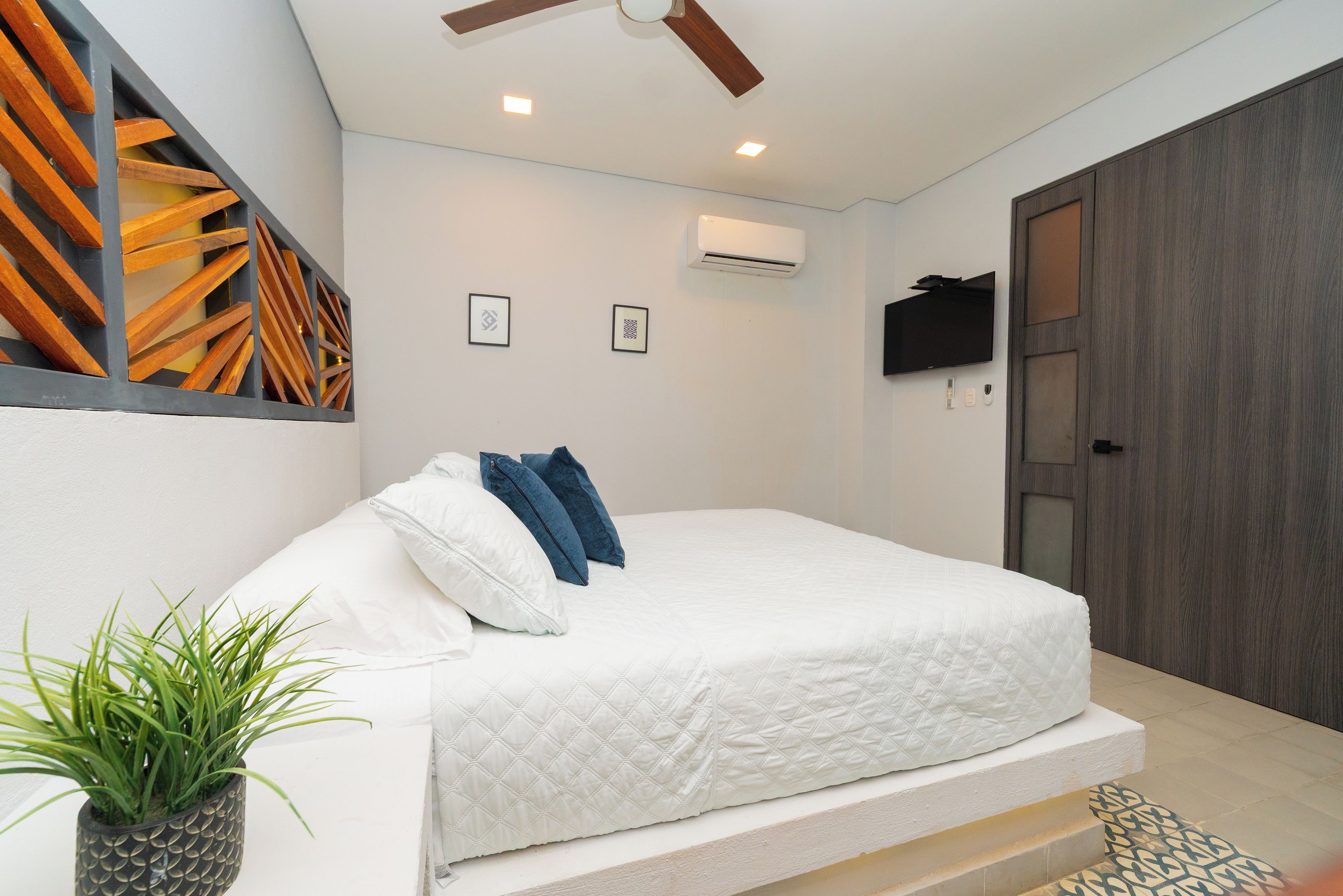 A bedroom with a bed, a ceiling fan, an air conditioning unit, a mounted TV, and a door.