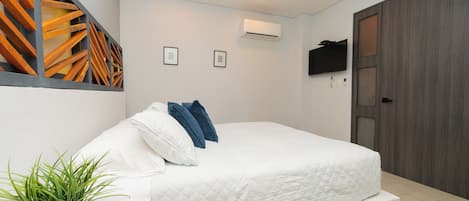 A bedroom with a bed, a ceiling fan, an air conditioning unit, a mounted TV, and a door.