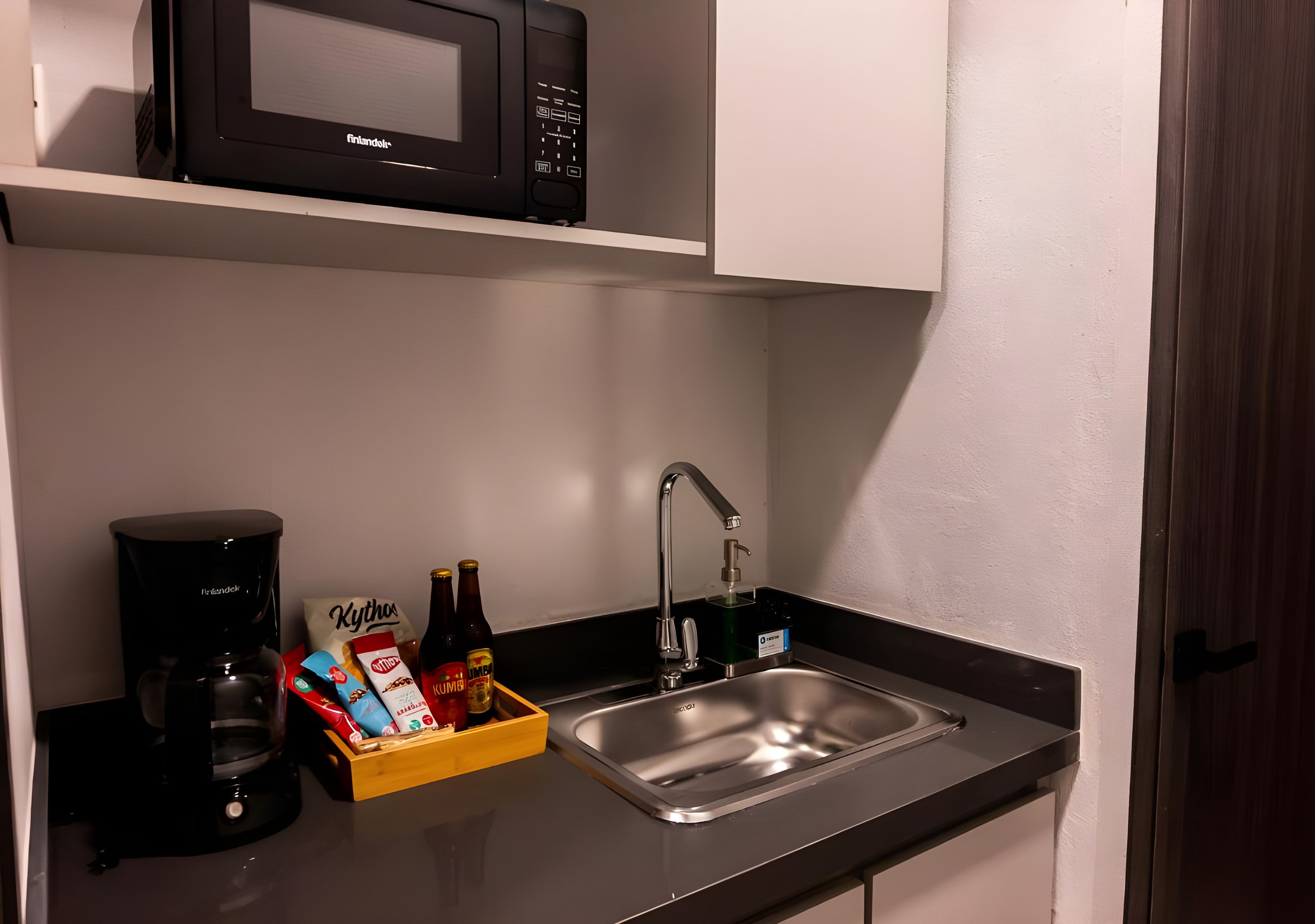 A kitchenette with a microwave, coffee maker, sink, and a box of snacks.