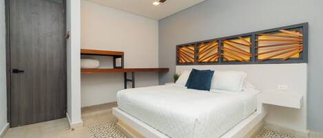 A bedroom with a bed, a ceiling fan, a wall-mounted shelf, and a patterned floor.