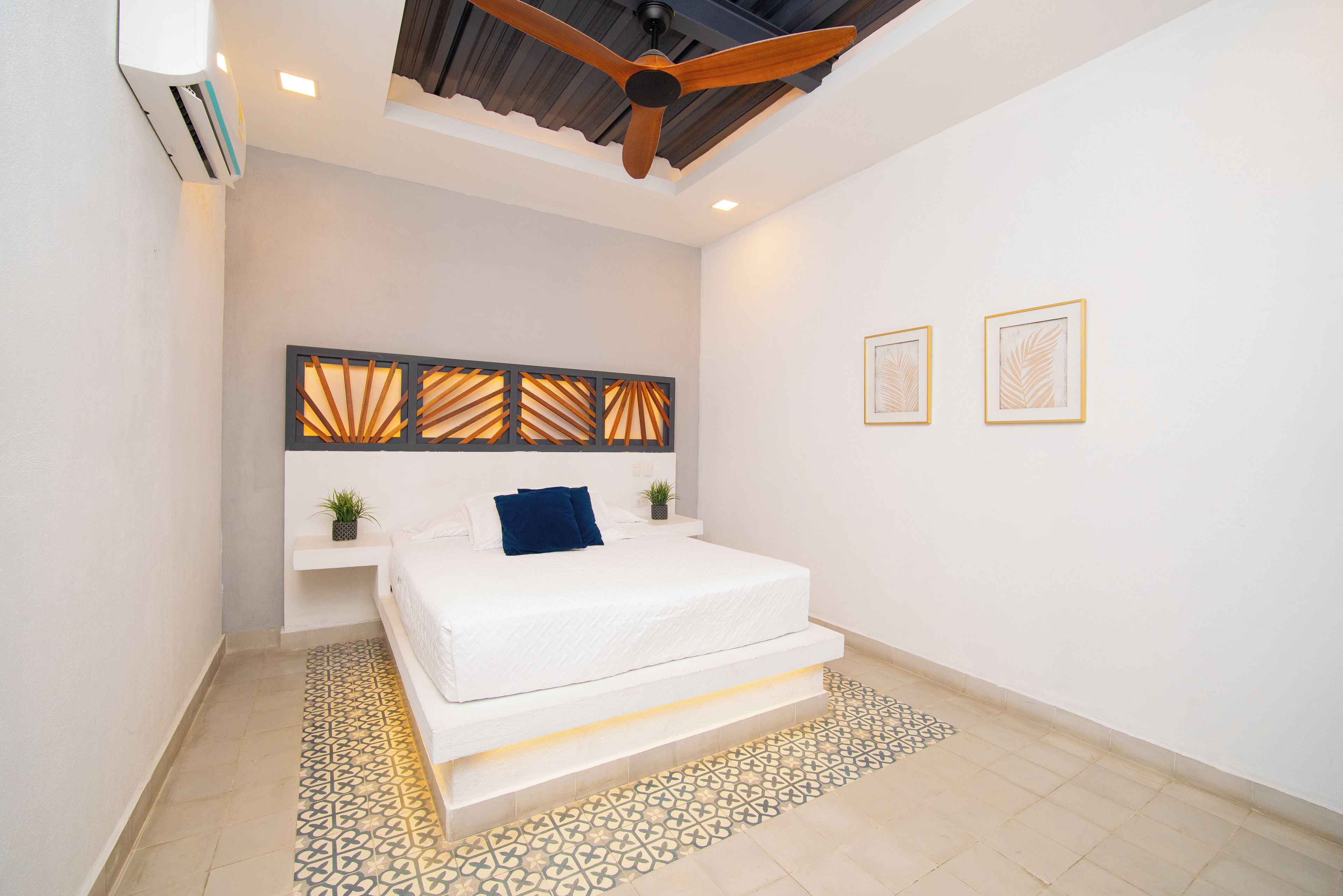 Une chambre à coucher moderne avec un lit, un ventilateur de plafond, un panneau décoratif mural et deux tableaux encadrés.