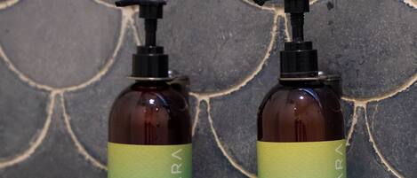Two bottles of shower gel with pump dispensers on a tiled wall.