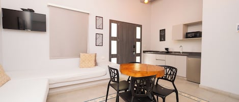 A compact living space with a dining area, kitchenette, and a seating area with a sofa and cushions.