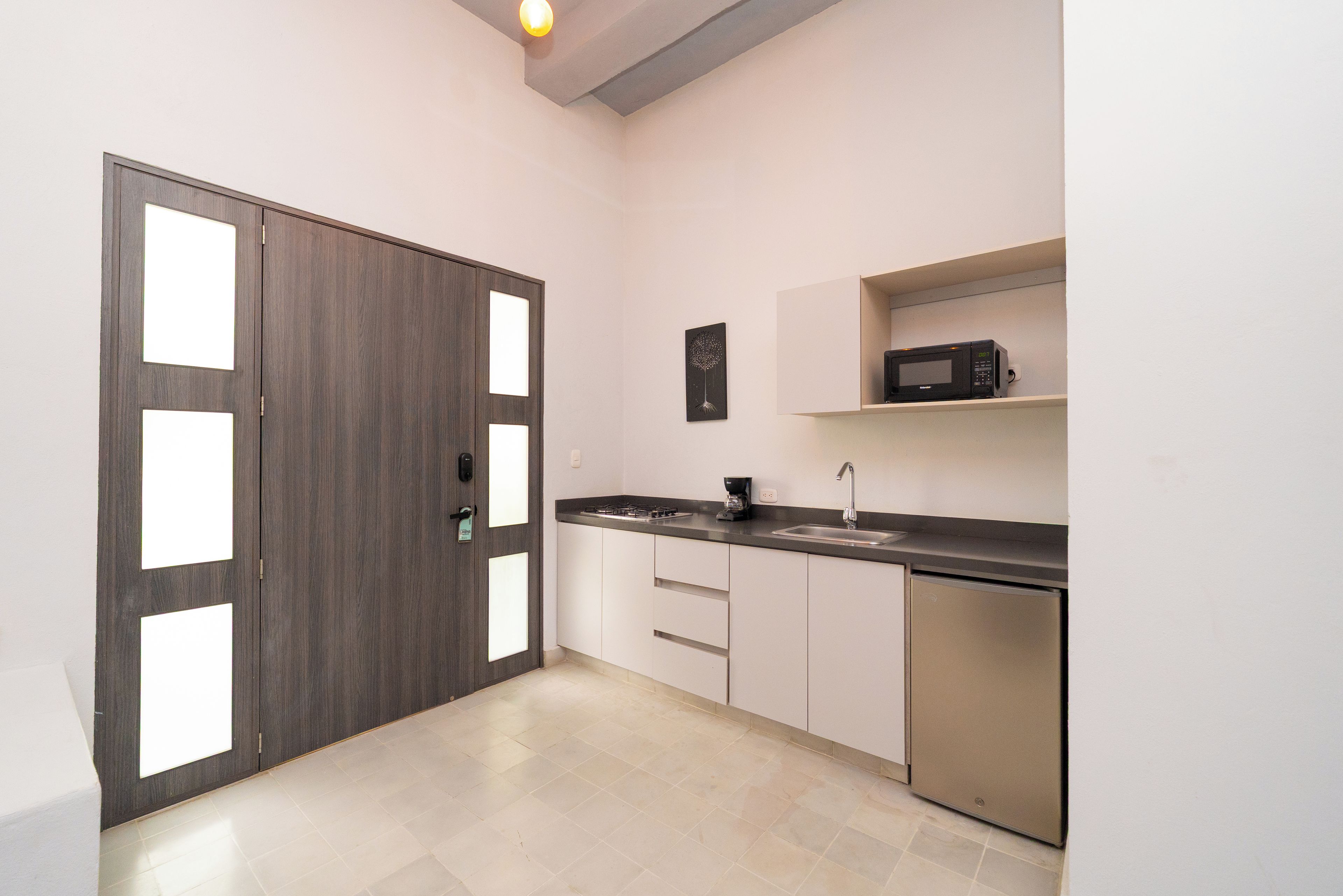 Een moderne keuken met een donker houten deur, witte kastjes, een roestvrijstalen spoelbak en een magnetron en koffiezetapparaat.