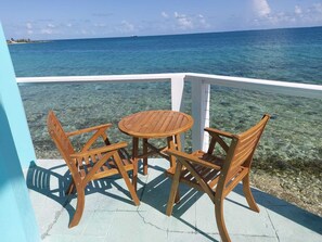 Un tavolo e delle sedie in legno su un balcone con vista sull'oceano.