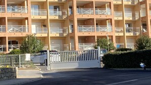 Un edificio de varios pisos con balcones, entrada protegida por una reja y zona de estacionamiento.