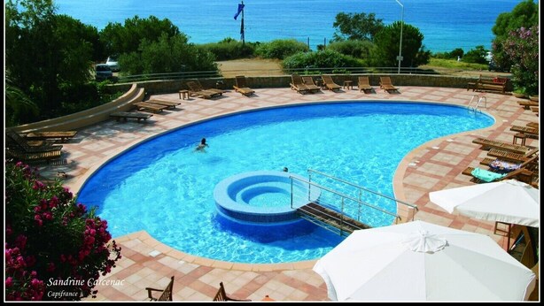 Una piscina con vistas al mar, rodeada de sillones de playa y sombrillas.