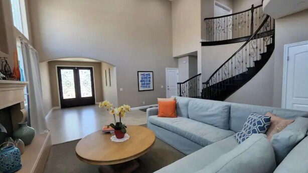 Ein geräumiges Wohnzimmer mit einem hellblauen Sofa, einem runden Holztisch und einer Treppe mit schwarzer Geländer.