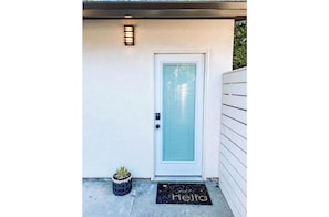 A white door with a frosted glass panel, a small potted plant, and a 'hello' mat on the ground. - East Park Studio | Downtown Style  (Chico)