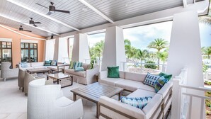 A spacious outdoor lounge area with multiple seating options, ceiling fans, and large windows offering views of palm trees and a beach. - 1804 Tropical Palms Circle (Kissimmee)