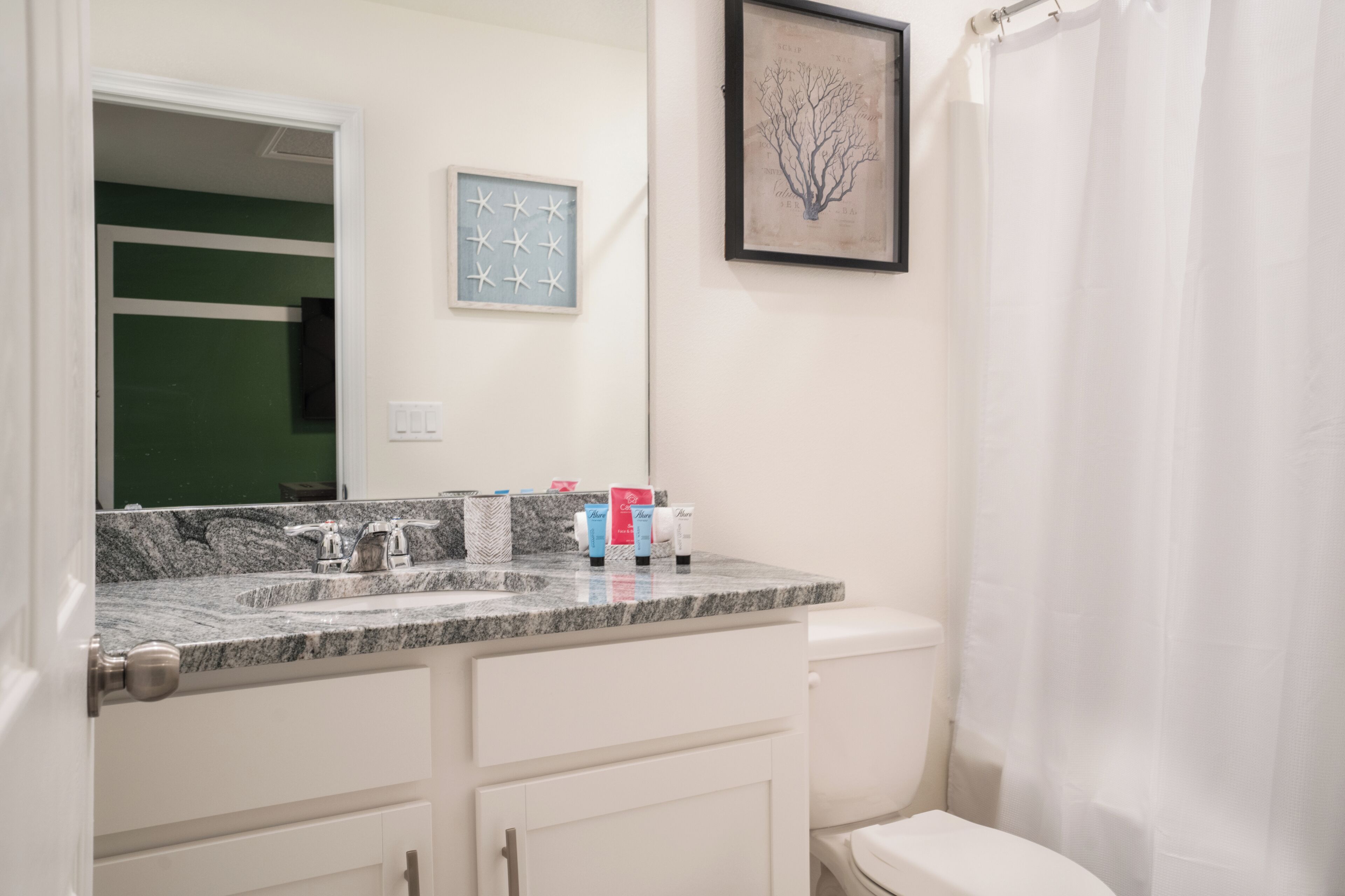 A bathroom with a marble sink, white cabinets, a framed picture, and a toilet.