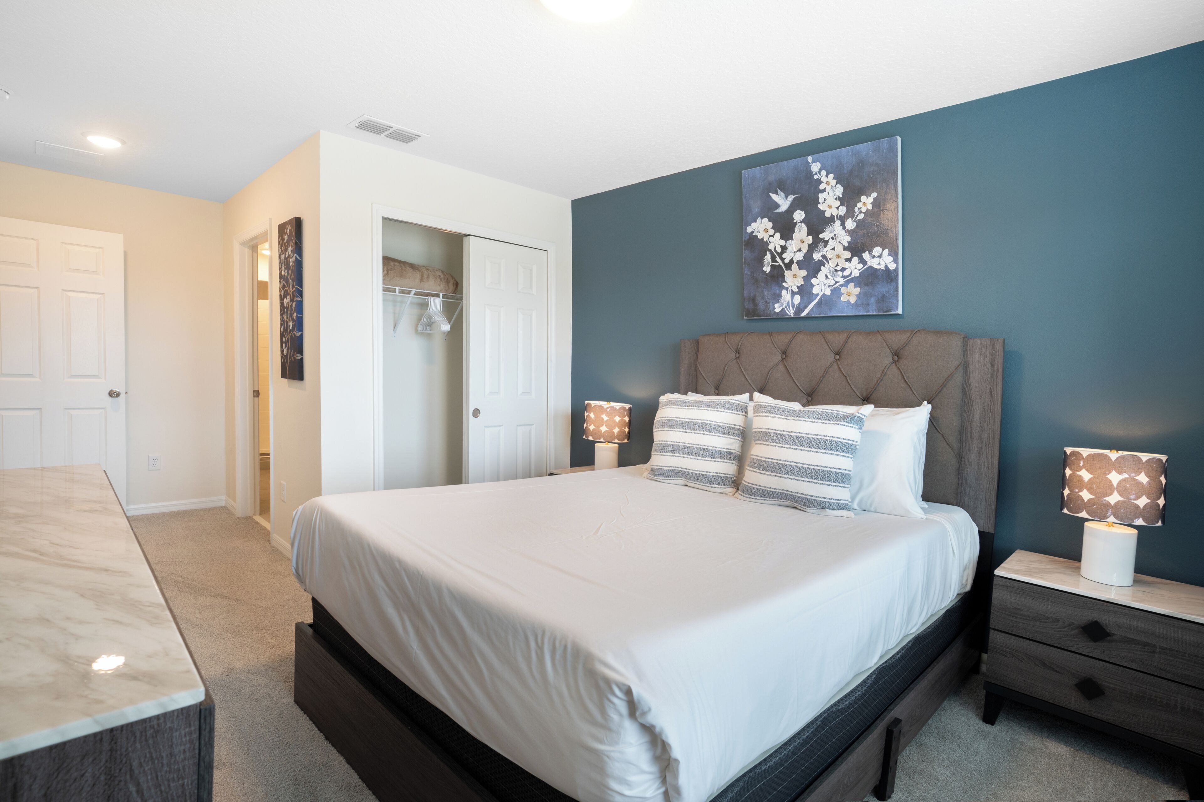 A bedroom with a large bed, bedside lamps, a headboard, and a wall-mounted artwork.