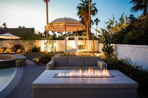 Un espace aménagé au bord de la piscine, avec un foyer, des chaises longues et un parasol.