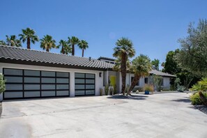 Ein modernes Haus mit Garage, Auffahrt und Palmen.