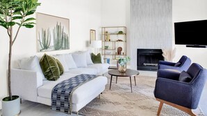 Een moderne woonkamer met een witte bank, een blauwe fauteuil, een salontafel en een boekenkast.