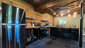 A modern kitchen with a stainless steel refrigerator, black appliances, wooden wall paneling, and a tiled floor.