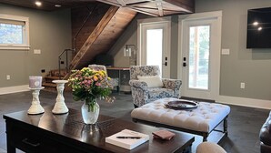 A spacious living area with a high ceiling, a staircase, a sofa, a coffee table, and a dining table.