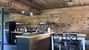 A modern kitchen with wooden walls, a central island, and a dining area with chairs.