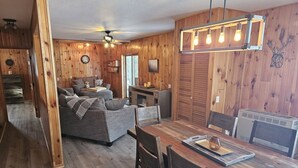 Interior acogedor de una cabaña con suelo de madera, un sofá, una mesa de comedor y una chimenea.