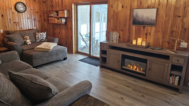 Una sala de estar acogedora con chimenea, paredes de madera y un ventanal grande.