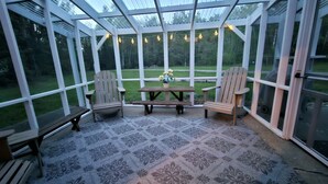 Un patio cubierto con mesa y sillas, amplias ventanas y vistas a un área verde.