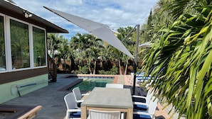 Un espace extérieur avec une piscine, une table et des chaises, entouré de palmiers et doté d’une terrasse en bois.
