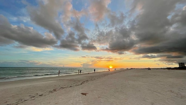 Une plage où l’on voit des empreintes de pas menant à l’eau, un coucher de soleil en arrière-plan et un ciel dégagé.