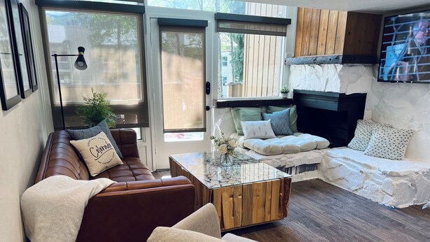 Een moderne woonkamer met een bruine leren bank, een beige fauteuil, een glazen salontafel en een witte stenen schoorsteen.