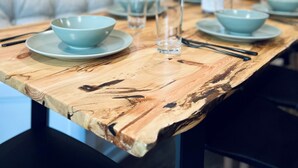 Een eettafel met lichtblauwe kommen en borden, een houten tafel met een opvallend houtpatroon, en een wand met een botanische afbeelding.