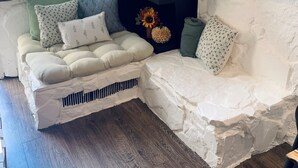Een gezellige woonkamer met een stenen openhaard, een hoekbank en een groot raam met uitzicht op de straat.