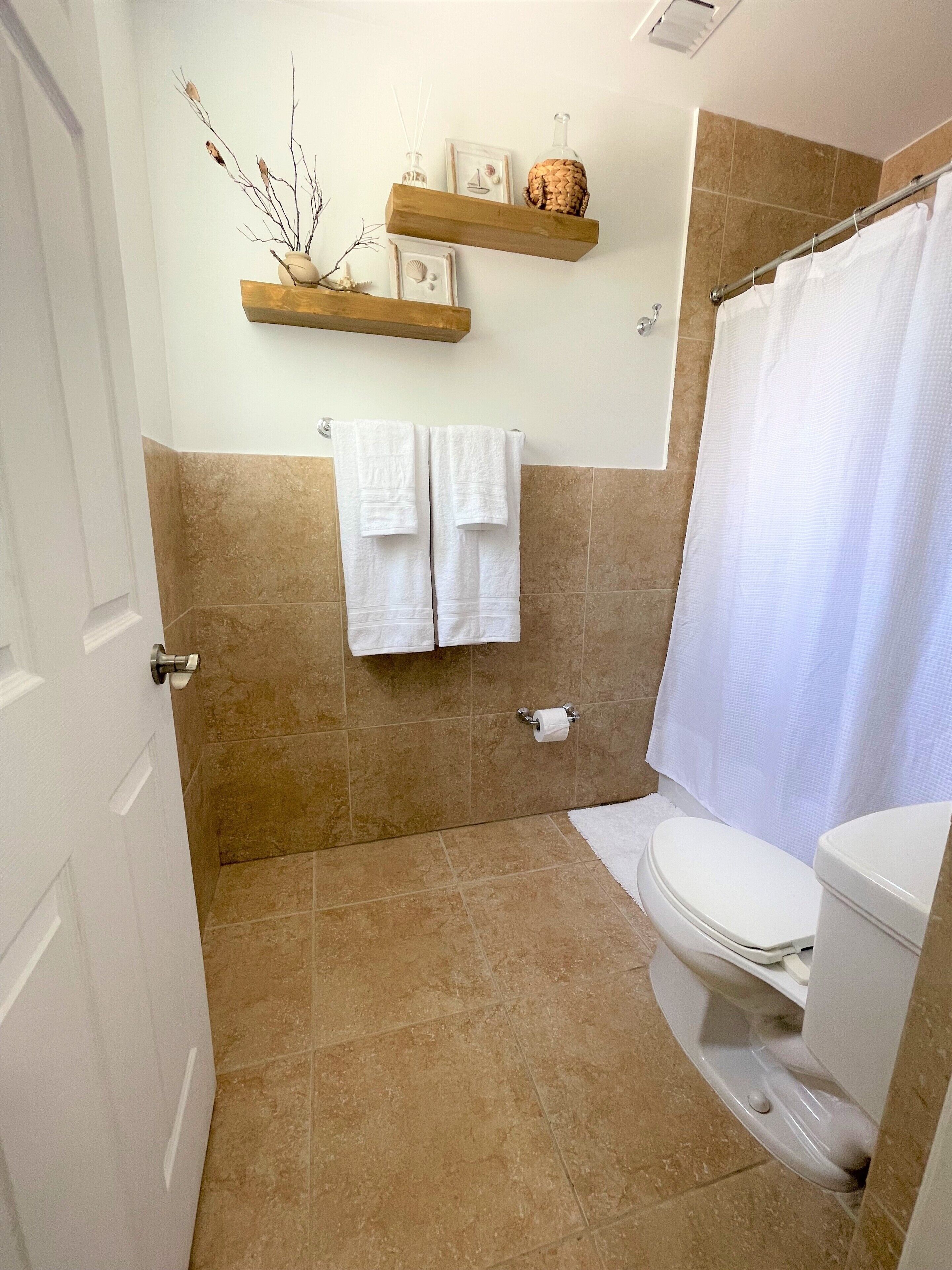 Une salle de bain avec des toilettes, un rideau de douche et deux serviettes accrochées au mur.